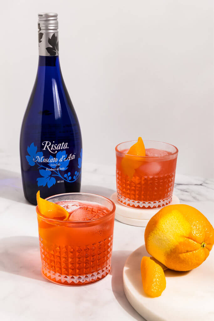 Risata Negroni decorated with orange slices and a Risata Miscato d'Asti Bottle